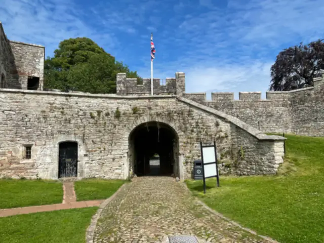 The stone gatehouse at Brougham Hall, a Union flag flying above its crenellated walls and a cobbled path leading through the arched entrance